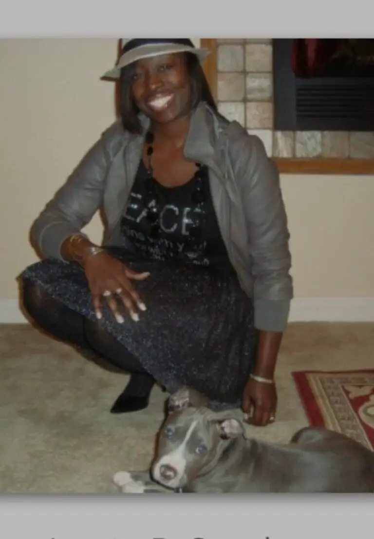 Person in black outfit with gray jacket and cat at feet indoors.