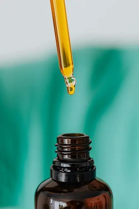 Close-up of an eye-dropper of essential oil dropping into a brown opaque bottle